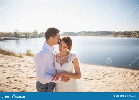 A Bride And Groom Are Standing On The Beach At Sunset With Their Reflection In The Wet Sand