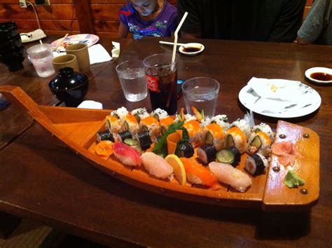 A Sushi Platter On A Wooden Table With People Sitting At The Table In The Background