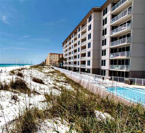 An Apartment Building On The Beach With A Swimming Pool And Sand Dunes In Front Of It