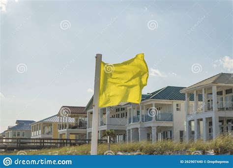 Yellow Warning Flag On A Pole Against The View Of Beach Houses And Sky